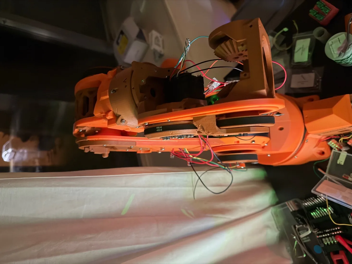 The orange arm laid out on a bench with its wiring exposed